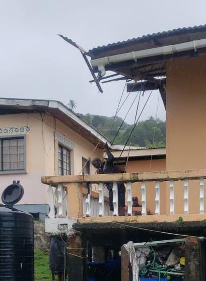 A man tries to tie a damaged roof in place in Delaford, Tobago on July 1. - 