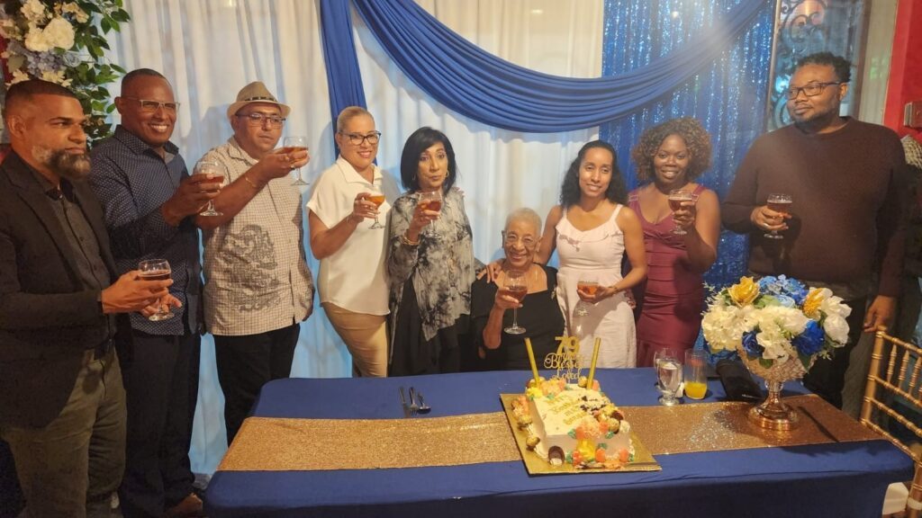 Toasting to Hilma Smith Barnes (seated): from left, Ancil Rooplal, Reynold James, Rajesh Ramsundar, Jan Charles, Amina Baksh, Curlin Alexander-Teelucksingh, Joanne Jordan, and Al Alexander. - 