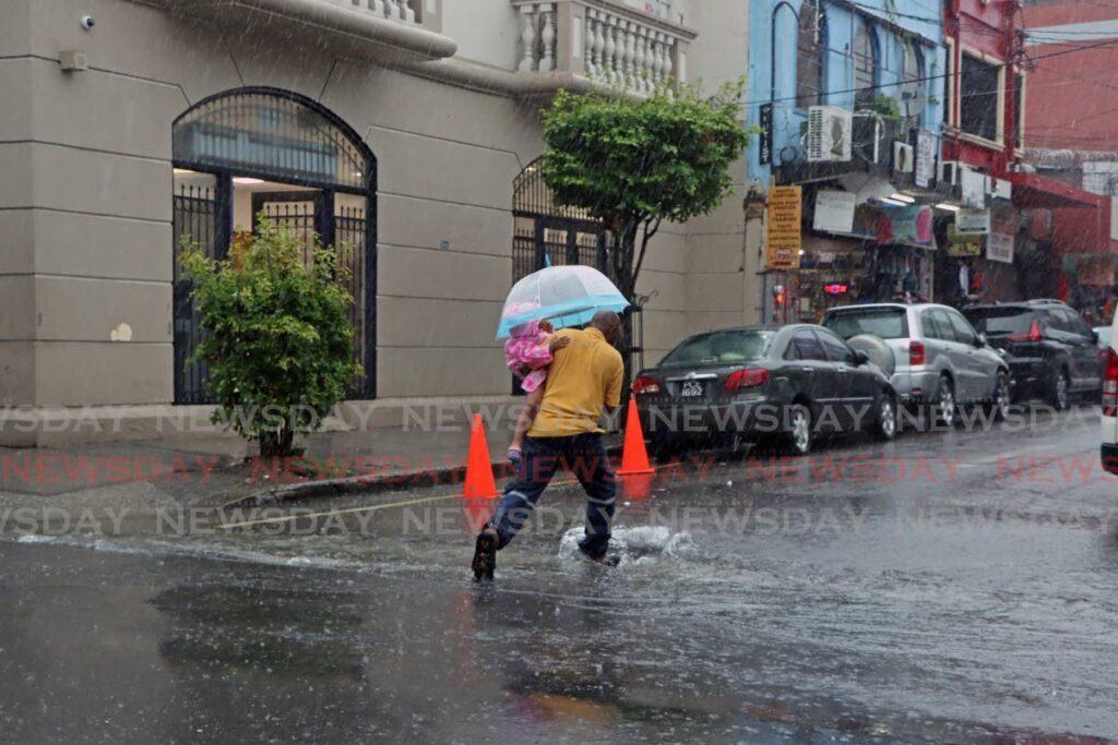 A man walks through floodwaters with a toddler on Henry Street, Port of Spain on August 12. - Photo by Venessa Mohammed