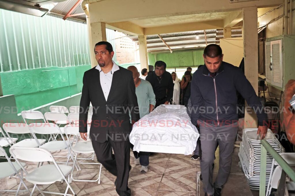 Sons Micah and Marcus Baksh carry the body of their father, cultural icon Walid Baksh, after his funeral at his Marabella home on August 12. - Photo by Lincoln Holder 