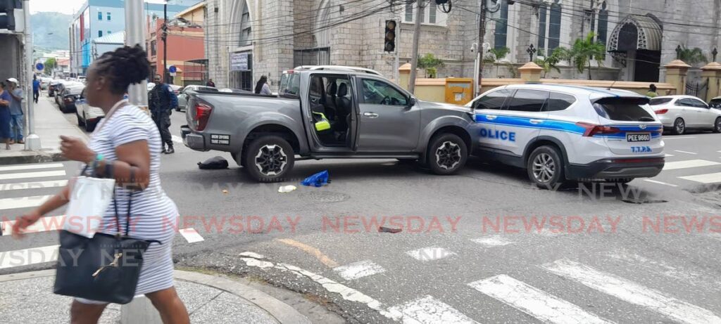 A woman walks by unfazed after police intercepted a stolen vehicle at the corner of Park and Henry Street in Port of Spain on August 15.  - Joey Bartlett