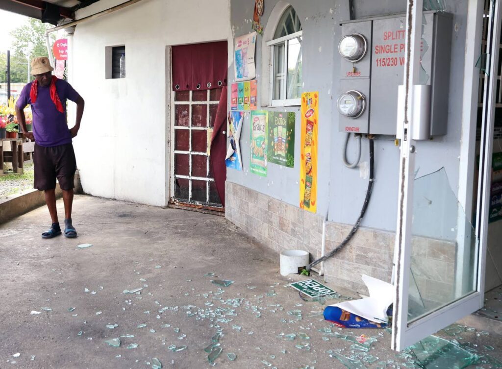 Andy Guerra, father of murder victim Enrico Guerra, who was shot dead along with his 5-year-old daughter, Anika, looks at shattered glass left behind by gunmen at the mini mart where the incident took place on August 21. - Photo by Venessa Mohammed