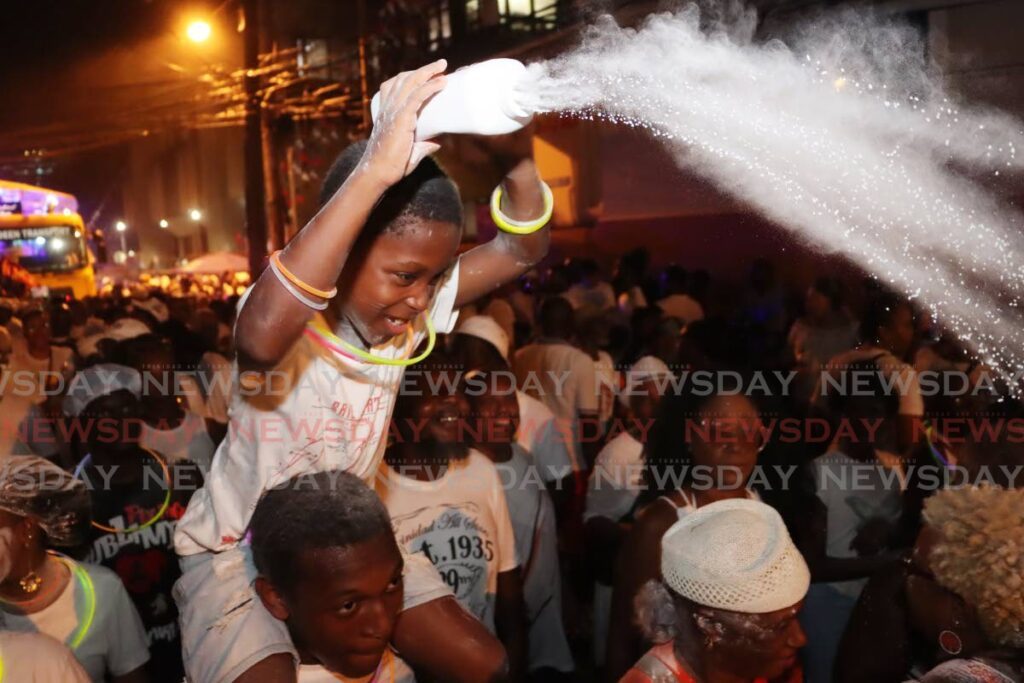 Xavion Raymond sprays powder on other pan lovers during the Pan and Powder Parade on Pembroke Street, Port of Spain. 