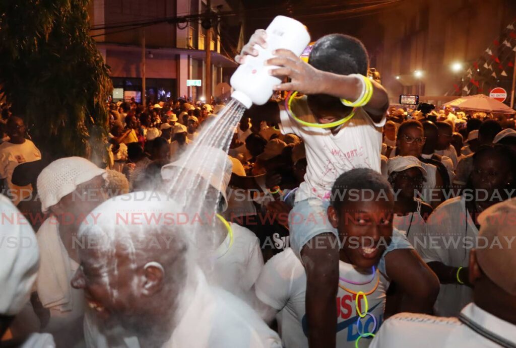 Xavion Raymond sprays powder on other pan lovers during the Pan and Powder Parade on Pembroke Street, Port of Spain. - Photo by Ayanna Kinsale