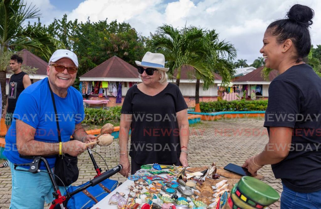 Tourist John Finkelstein tests out his chac-chacs, bought from vendor Mona Singh, right, while his wife Merle looks on in amusement, at Store Bay Beach Facility. - File photo by David Reid