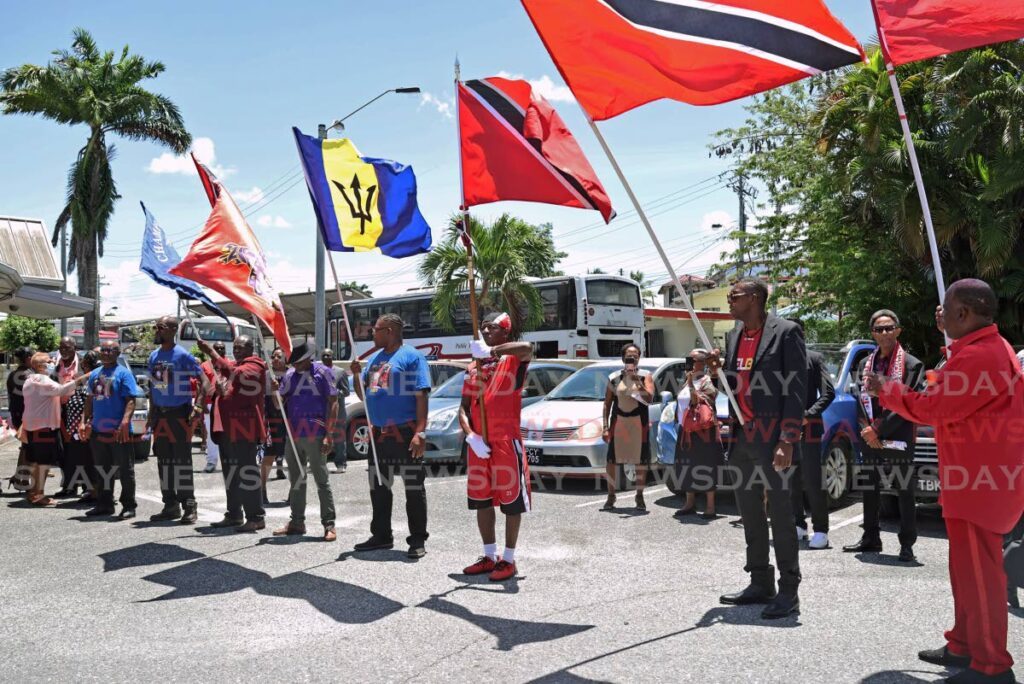 KEEPING THE FLAG FLYING: Grand send off for the late Joey Richardson, also known as the flagman, at his funeral at the St Phillip and St James RC Church in Chaguanas on September 4. Men raise their flags as the casket is carried out of the church. - Photo by Venessa Mohammed