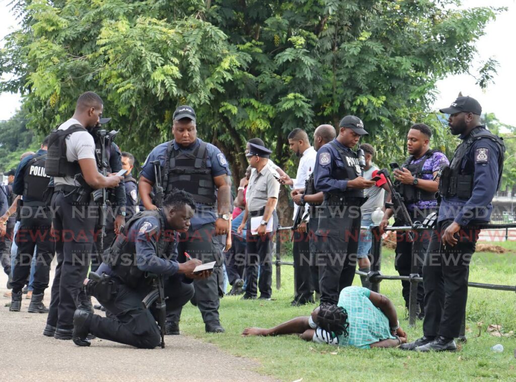 A police officer takes notes as he questions a man held after he evaded a roadblock, crashing into a car on the corner of Jerningham Avenue and Queen's Park East, Port of Spain on September 14. - Photo by Faith Ayoung