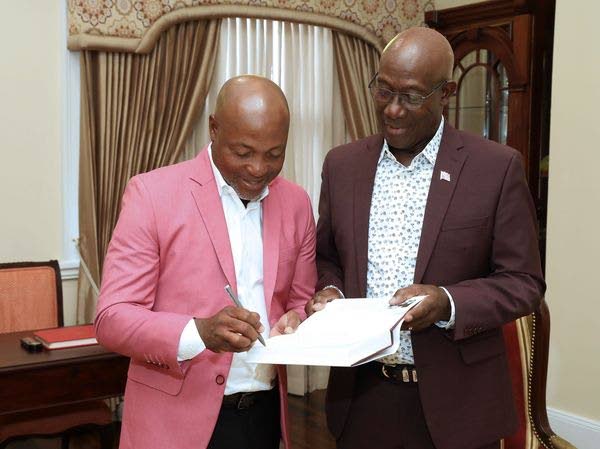 Brian Lara, left, signs a copy of his book for Prime Minister Dr Keith Rowley. - Photo courtesy Office of the Prime Minister's Facebook Page