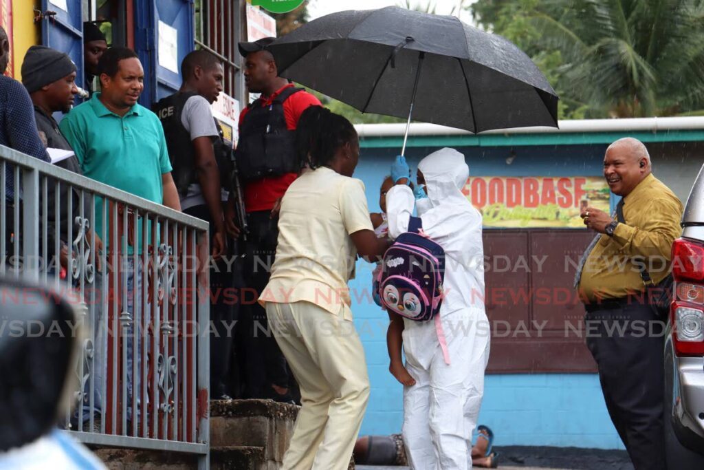 IN SAFE HANDS: Since it was still an active crime scene, a crime scene officer had to collect and then hand over a child to her relative outside Roxann's Learning and Childhood Centre in Malick, Barataria on Wednesday, hours after a shooting incident left two men dead and three others wounded. - Photo by Faith Ayoung