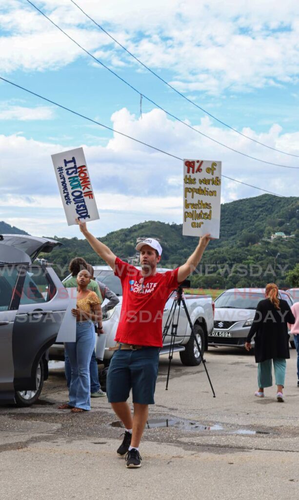 The IAMovement's cofounder Jonathan Barcant lifts up two signs during the organisation's climate awareness protest at the Queen's Park Savannah on September 26. - Photo by Gabriel Williams