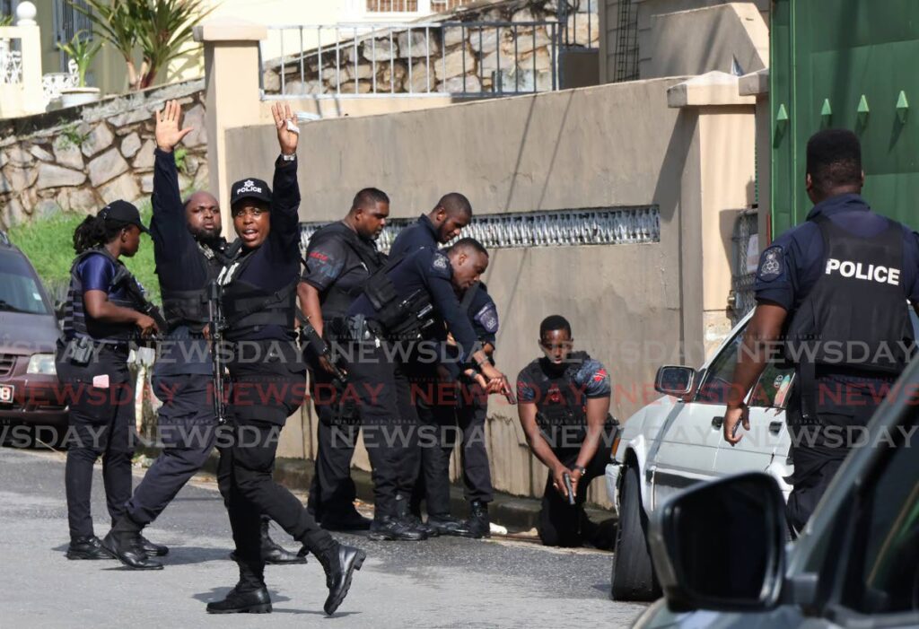 DRAMA IN BELMONT: Policemen, their guns drawn, guard the entrance to a manhole while collegues direct drivers to stop during a dramatic manhunt near the St Francois Girls' College on Friday. Two suspects were later flushed out of the drains by officers. - Photo by Roger Jacob