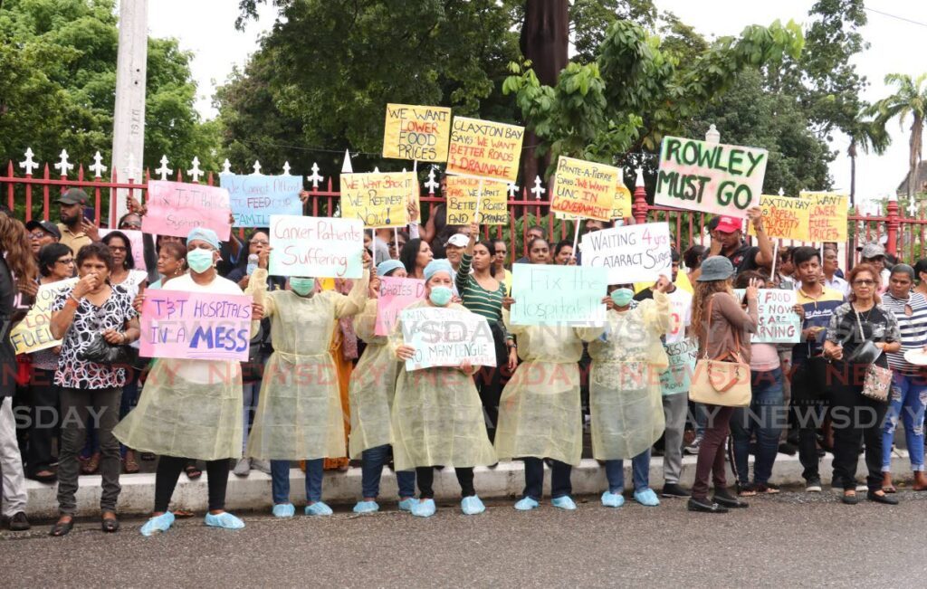 Protesters dressed in surgical gowns stand show their placards.  - Photo by Faith Ayoung