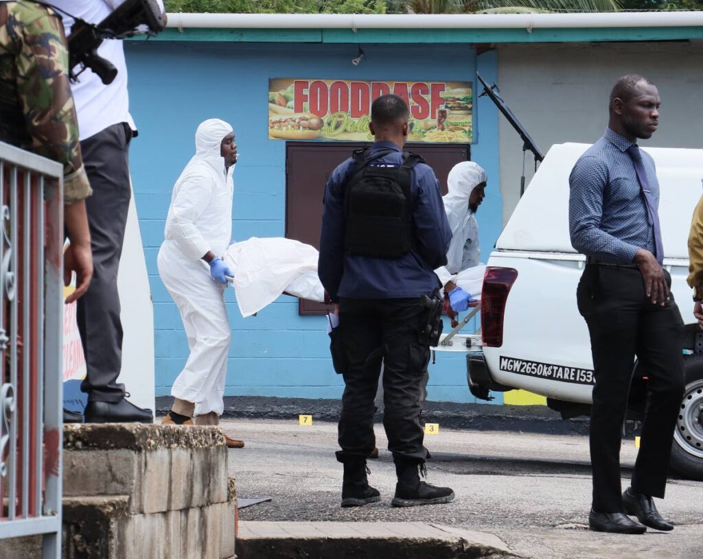 In this file photo, crime scene investigators remove the body of Gerald Caliste, who was killed by gunmen outside of Roxann's Learning and Childhood Centre, Malick, on September 25. - Photo by Faith Ayoung