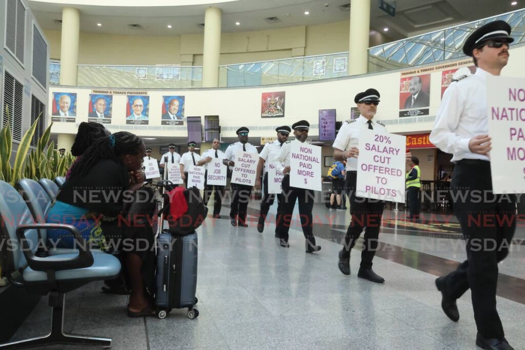 While passengers sit and watch, Caribbean Airlines Ltd (CAL) pilots march with their placards on Thursday morning inside Piarco International Airport. - Photo by Roger Jacob