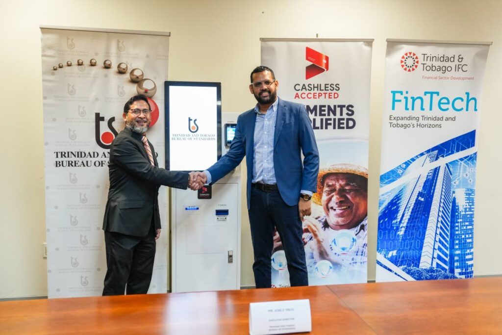 Josè E Trejo, executive director, TTBS, shakes hands with John Outridge, CEO of TTIFC to formalise the MoU signing at TTIFC office in front of a payment kiosk. - 
Photo courtesy TTIFC
