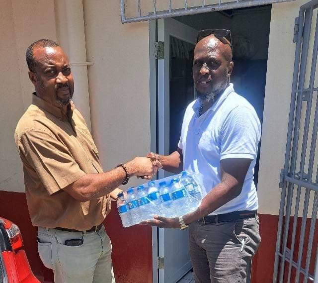 A Mighty Krush Entertainment representative, right, gives cases of water to a Delaford Anglican Primary School teacher.  - 