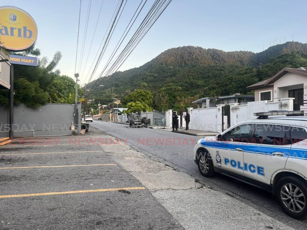 Police keep watch over a vehicle that overturned after hitting a wall at the end of a police chase on Majuba Cross Road, Petit Valley, on October 18. The vehicle is believed to have been stolen. - Photo by Sydney Joseph