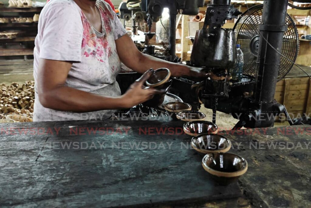 A worker at Potters Hand, Edinburgh, Chaguanas, using a machine to press the clay into the shape of a deya. Used engine oil is used to lubricate the machine so the clay does not stick. - Photo by Lincoln Holder 