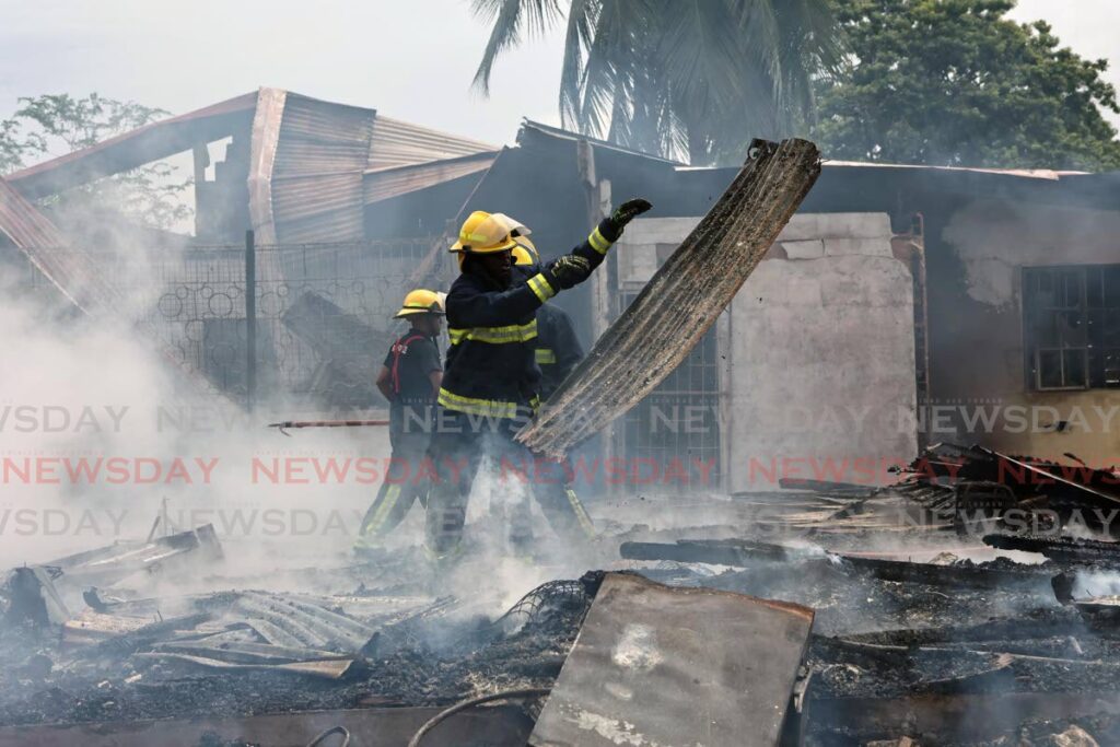 A fireman throws a burnt sheet of galvanise at the site of the defunct La Brea Lake Asphalt Sports club which was gutted by fire on October 22. - Photo by Lincoln Holder 