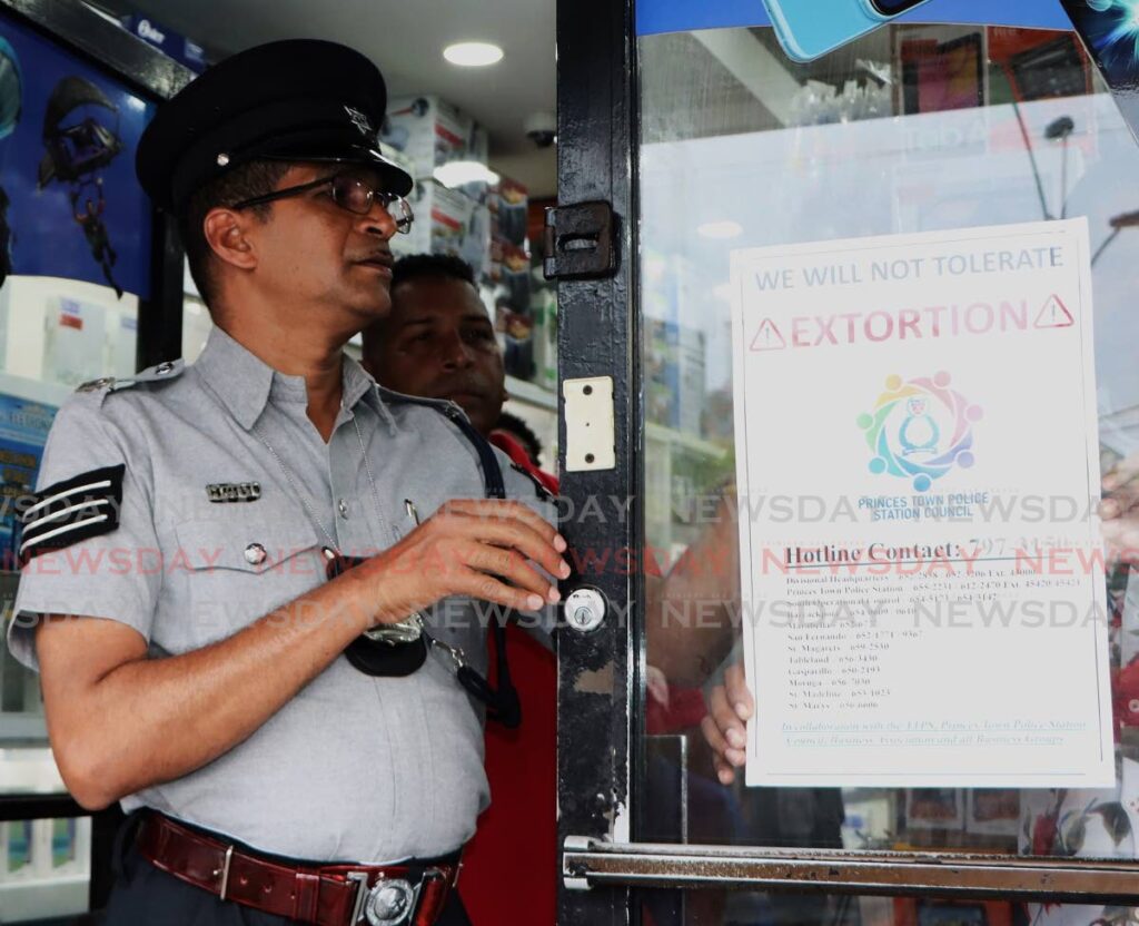 BE INFORMED: Acting Inspector Shaheed Mohammed sticks an anti-extortion flyer to the glass door of a businessplace in Princes Town on Thursday during a police walkabout. - Photo by Angelo Marcelle