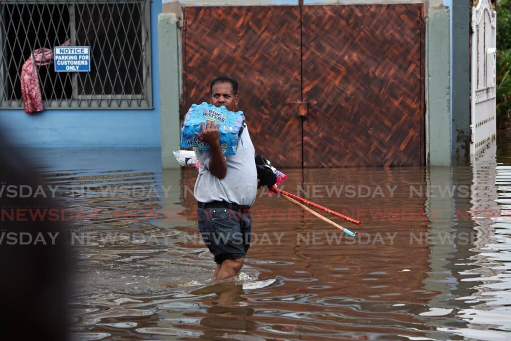 A resident hugs drinking water and cleaning supplies as he makes his way along a flooded Lachoos Road in Penal on Wednesday. - Photo by Lincoln Holder 