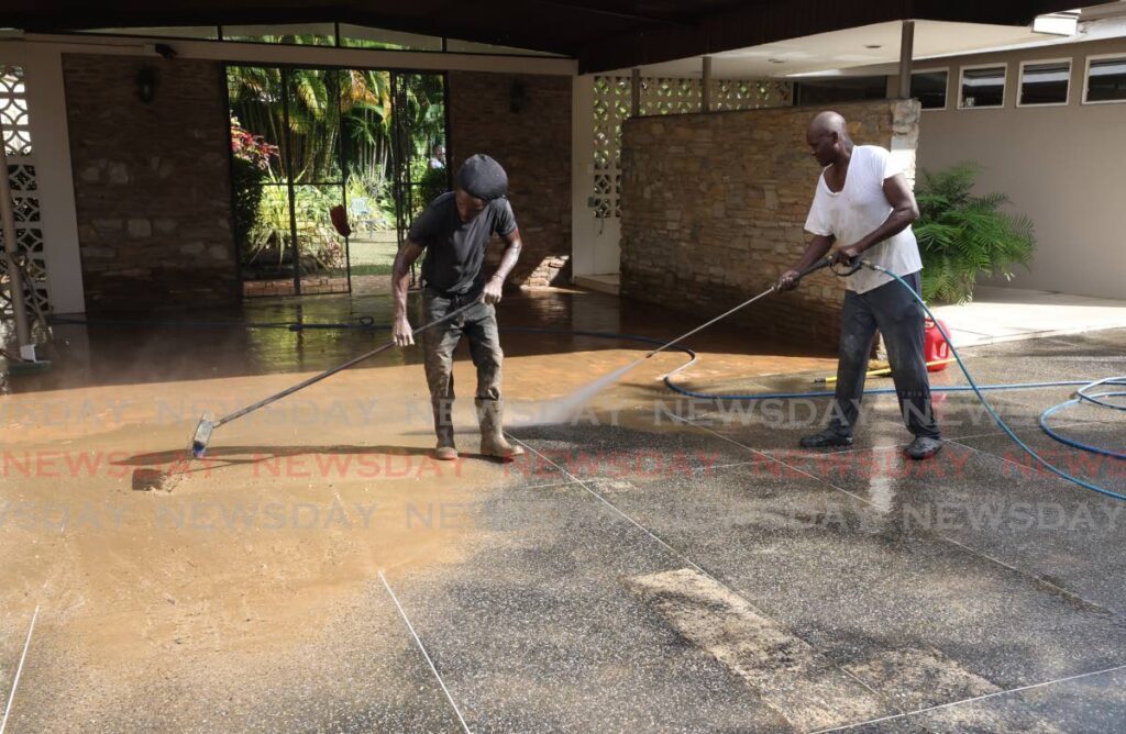 Workers powerwash a driveway  covered with silt a day after heavy rainfall caused flooding on Saddle Road, Maraval, on November 24. - Photo by Faith Ayoung