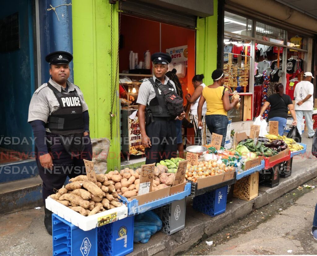 You would be wrong if you thought these two policemen were selling agriculture produce on Charlotte Street, Port of Spain. The fact is that were on patrol on November 26, keeping an eye out for anyone seeking to rob vendors. - Photo by Faith Ayoung