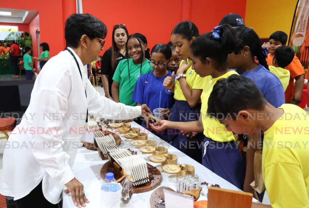 Cherie-Anne Ramlakhan, of Kairi Chocolate Company Ltd, left, gives chocolate samples to students of Grant Memorial Presbyterian School. - Photo by Faith Ayoung