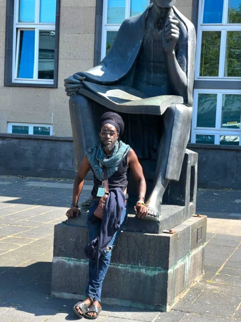 Dr Charleston Thomas lounging on a statue in the university of Vienna, Austria, after giving a presentation. - Photo courtesy Dr Charleston Thomas.