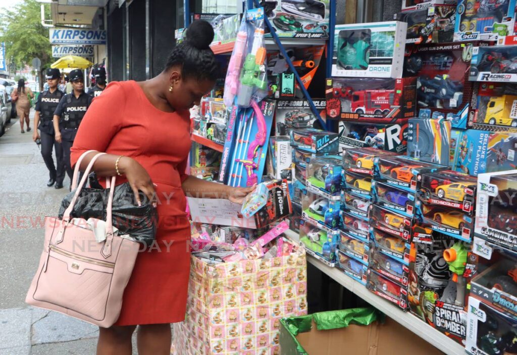 As a woman takes interest in a toy being sold on Frederick Street, Port of Spain on December 13, police officers can be seen in the background on patrol. - Photo by Angelo Marcelle