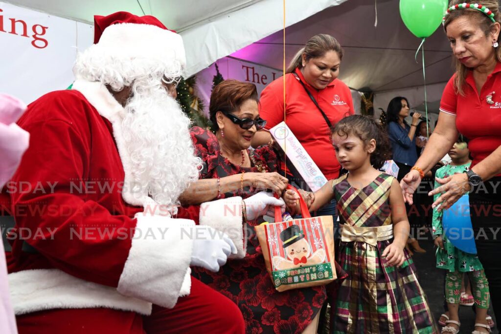 Opposition Leader and Siparia MP Kamla Persad-Bissessar, second left, assists Santa as he  distributes gifts during Christmas celebrations at her constituency office in Penal on December 14.  - Lincoln Holder 