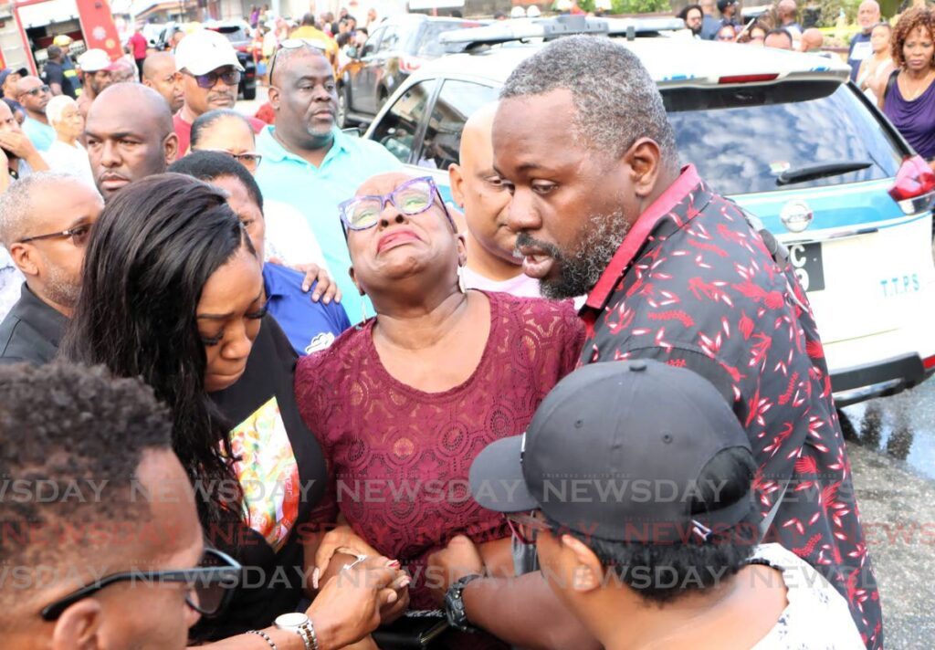 CAMILLE'S PAIN: Housing Minister Camille Robinson-Regis weeps as she is supported outside the home of her Cabinet colleague Lisa Morris-Julian, who died in a fire on December 16.  - Photo by Angelo Marcelle