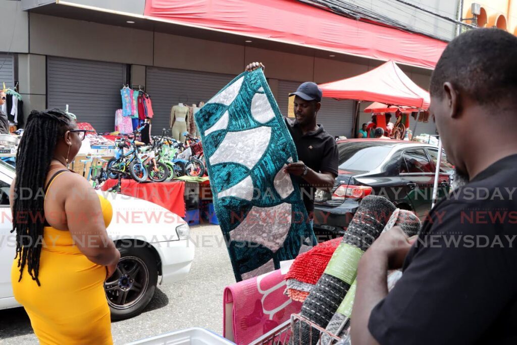 A vendor shows his customer his mats for sale on Charlotte Street, Port of Spain, Sunday. - Ayanna Kinsale