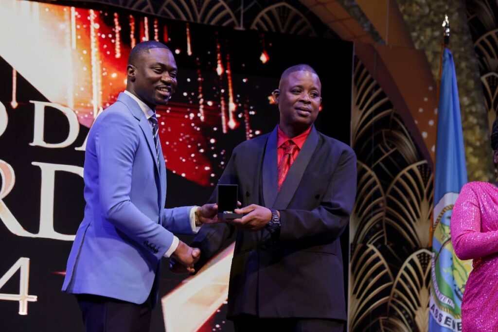 Mason Hall Police Youth Club president Dexter Edwards, right, collects an award from Chief Secretary Farley Augustine earlier this month.  - 