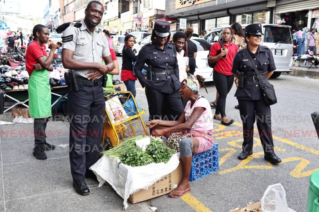 Police officers caution a celery and chive vendor who is blocking the entrance to Carlton Centre from High street, San Fernando on December 23. - Photos by Lincoln Holder