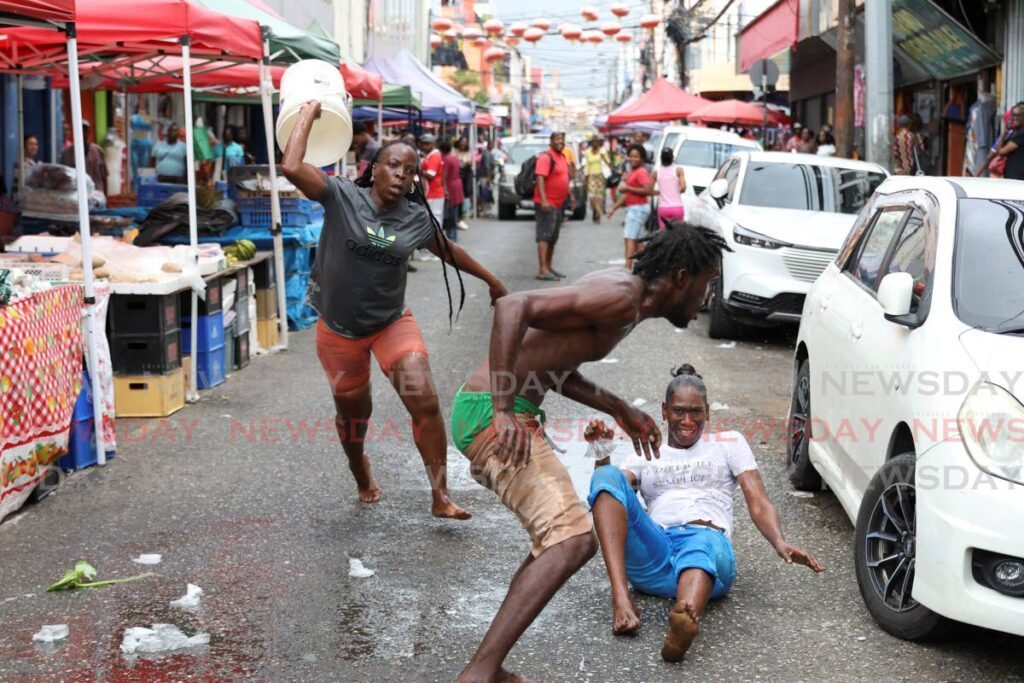 DOWN BUT NOT OUT: This vendor was all smiles when she realised her male adversary would be bested by another woman during a water fight on Charlotte Street on December 28.  - Photo by Jeff K Mayers