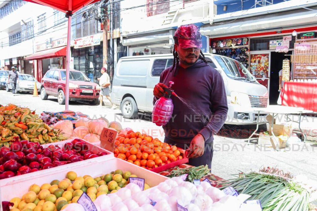 Street vendor Shermarke Edwards sprays water on his produce to keep it fresh at his stall on Charlotte Street, Port of Spain. - FILE PHOTO