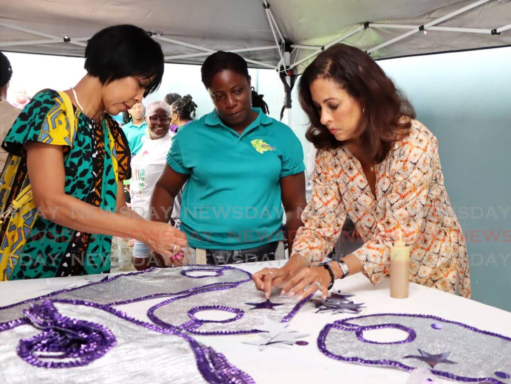 Sharon Clark-Rowley, wife of the Prime Minister, left, and US Ambassador to TT Candace Bond, right, apply patterns to costumes during the Zebapique mas camp meet and greet at Petit Valley on January 11. - Ayanna Kinsale