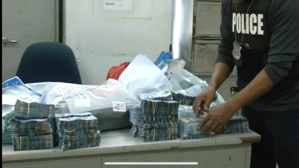 In this screenshot taken from a police video, a police officer at the Arouca Police Station secures over $2 m in cash which was seized during a search at a house on Huggins Street, Tacarigua on January 6. - 