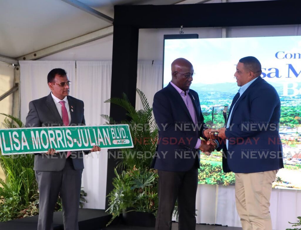 The Prime Minister, centre, greets Daniel Julian, widower of the late D'Abadie/O'Meara MP Lisa Morris-Julian, before presenting him with a Lisa Morris-Julian Blvd street sign, held by Works Minister Rohan Sinanan, at a commisioning ceremony in Arima on February 26. The road was formerly named the O'Meara Road. -  Photo by Ayanna Kinsale