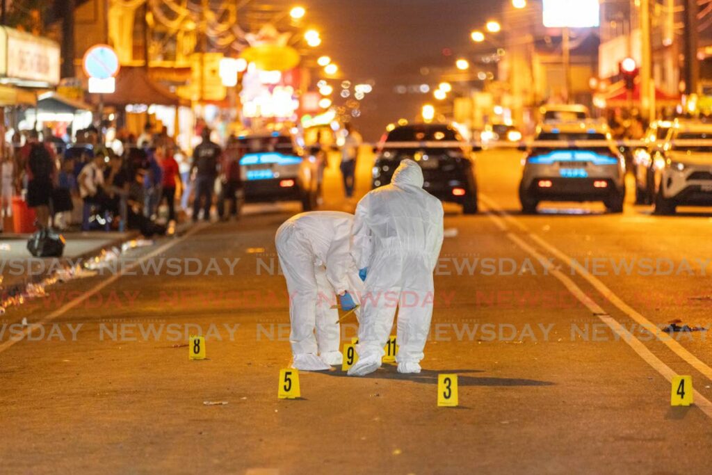 Officers examine the murder scene for possible evidence where one man was shot dead and three others wounded on the Western Main Road, St James on March 4. - Photo by Jeff K Mayers