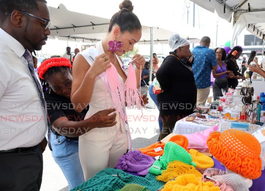 Daniel Austin, Xtra Foods CEO, looks on as founder of Krochet Kloset, Geanna Cunningham helps Miss World TT Anna-Lise Nanton try on a crotchet top at her booth at the  Xtra Foods Health, Beauty and Safety Fair. - Photos by Faith Ayoung